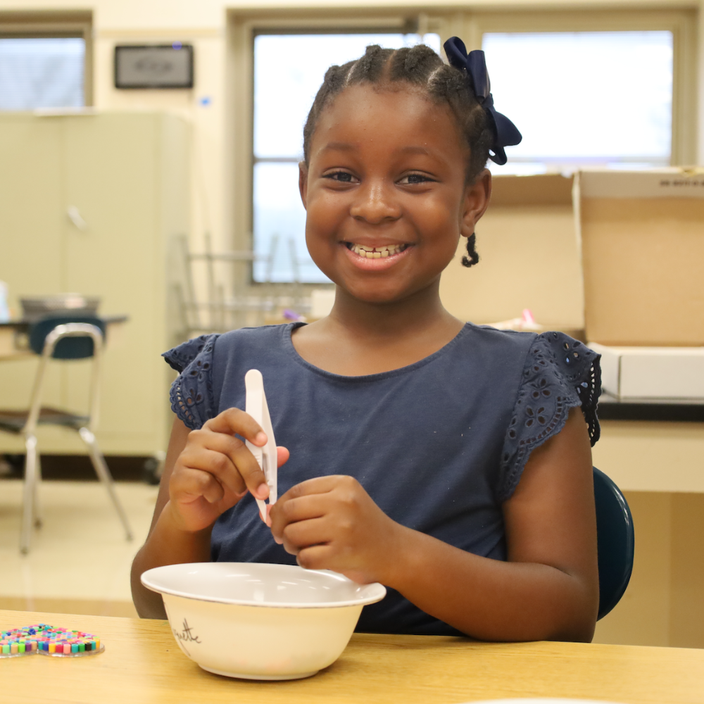 student with a blue shirt placing beads into a white bowl 