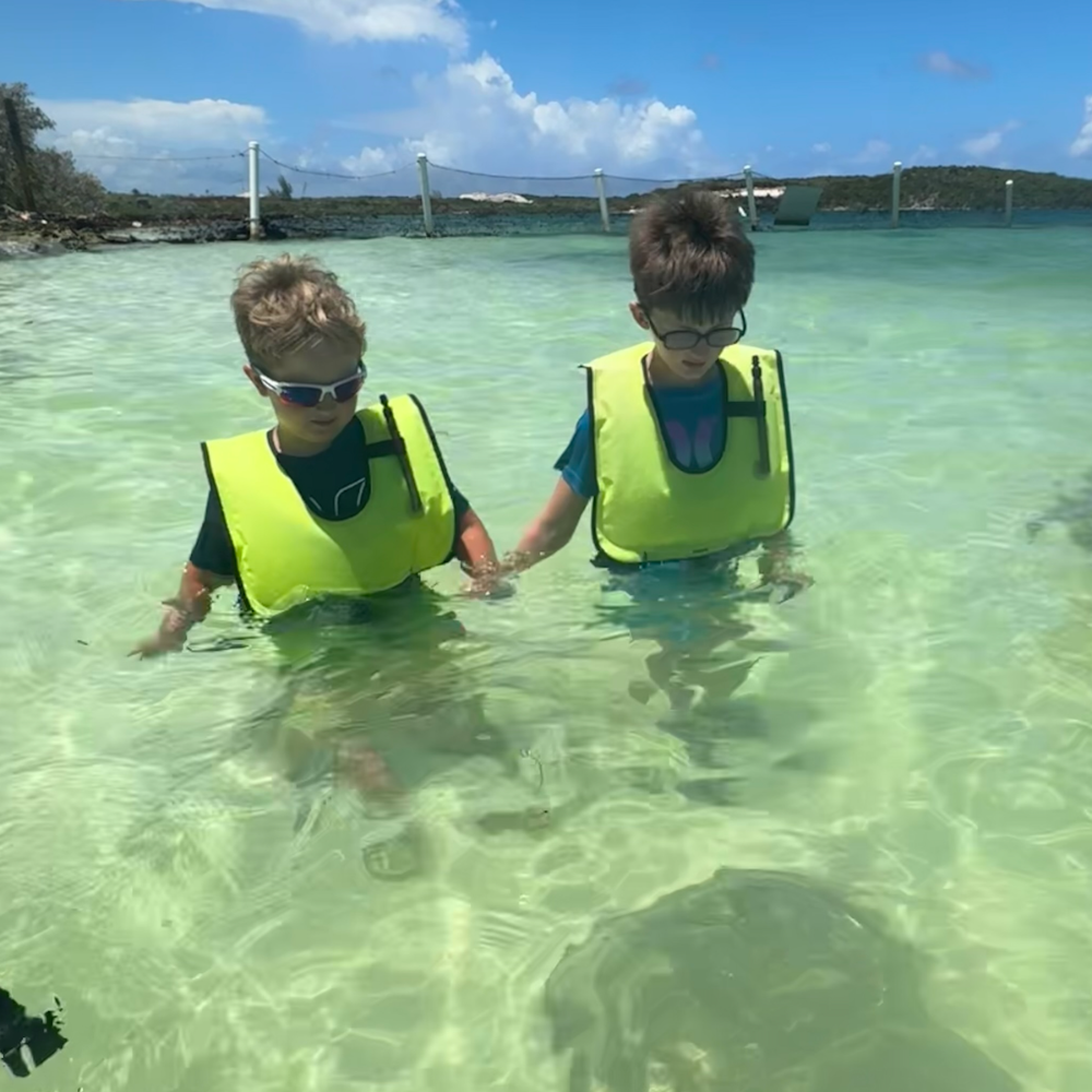 two boys with yellow life jackets standing in the water