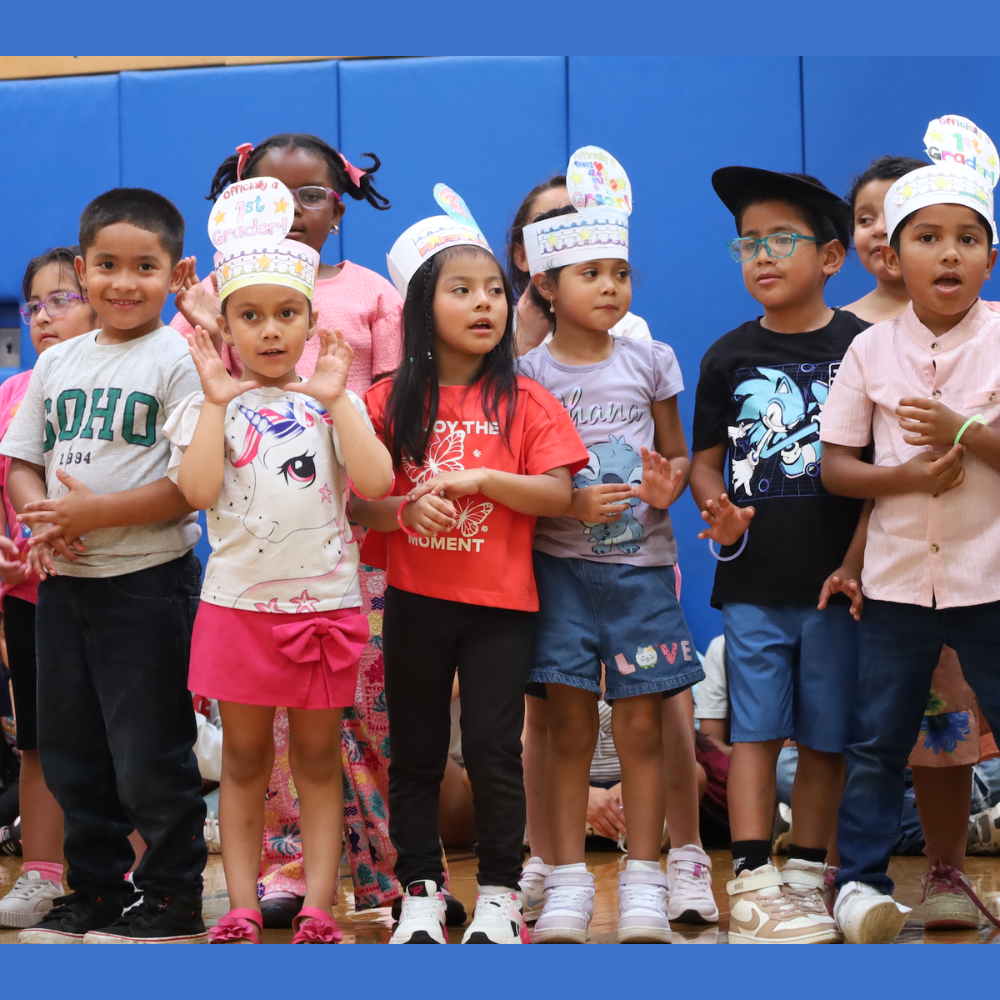 students wearing paper hats and singing in a gym 