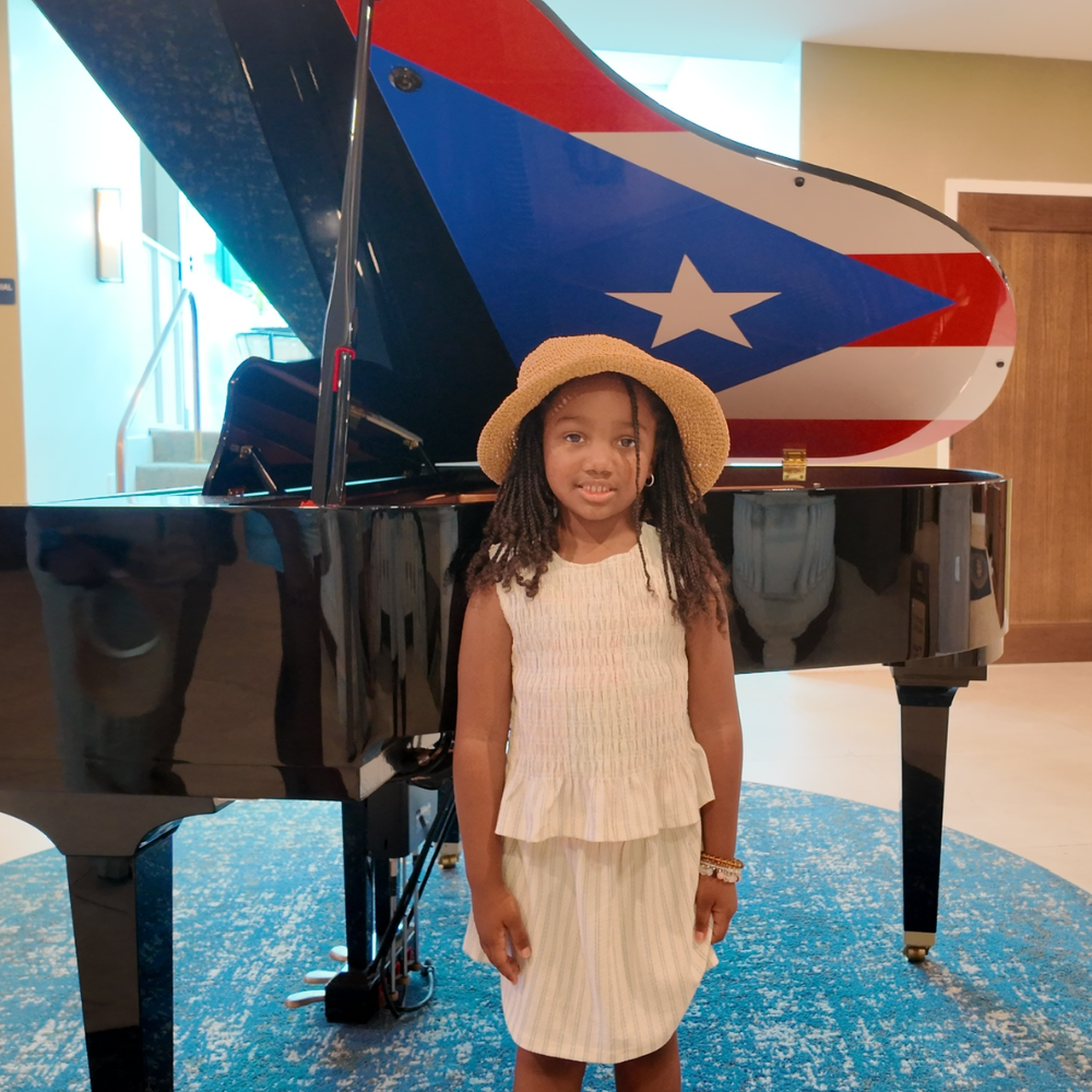 girl with a brown hat standing in front of a piano with the puerto rican flag