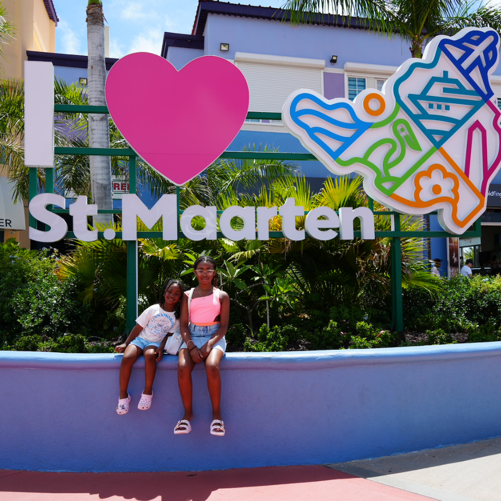 I love St. Maarten sign with two girls sitting on a blue wall 
