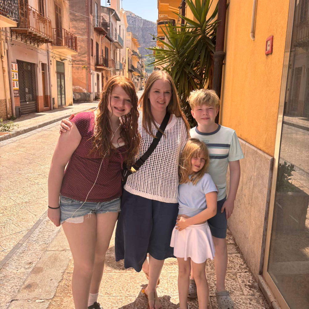 four people standing on a street with a large green plant behind them