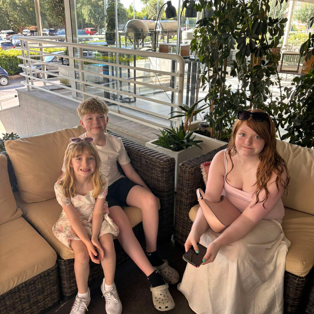 three students sitting on a couch with a large plant behind them