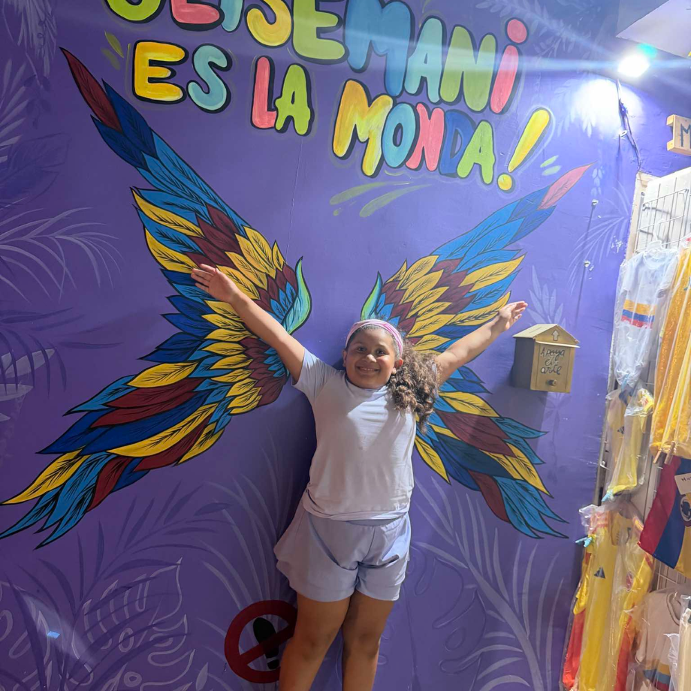 A girl standing in front of a painting of wings. 