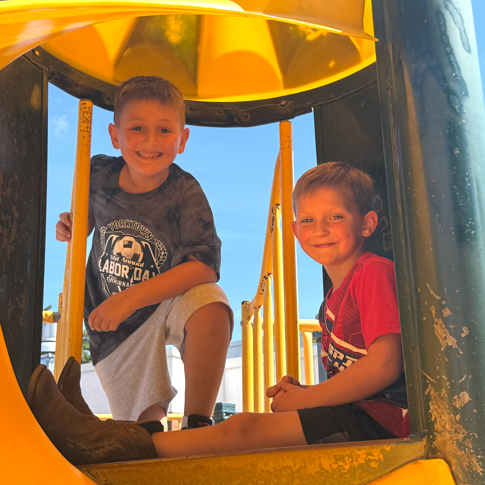 two students standing on top of a yellow slide