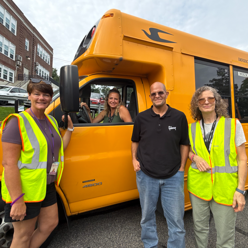 three people standing one person sitting in a school bus
