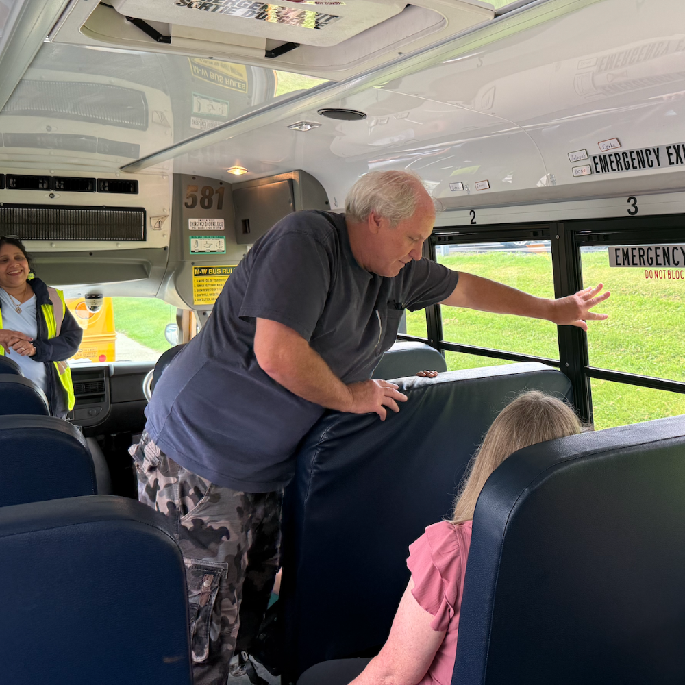 man standing over students showing an emergency exit on a school bus