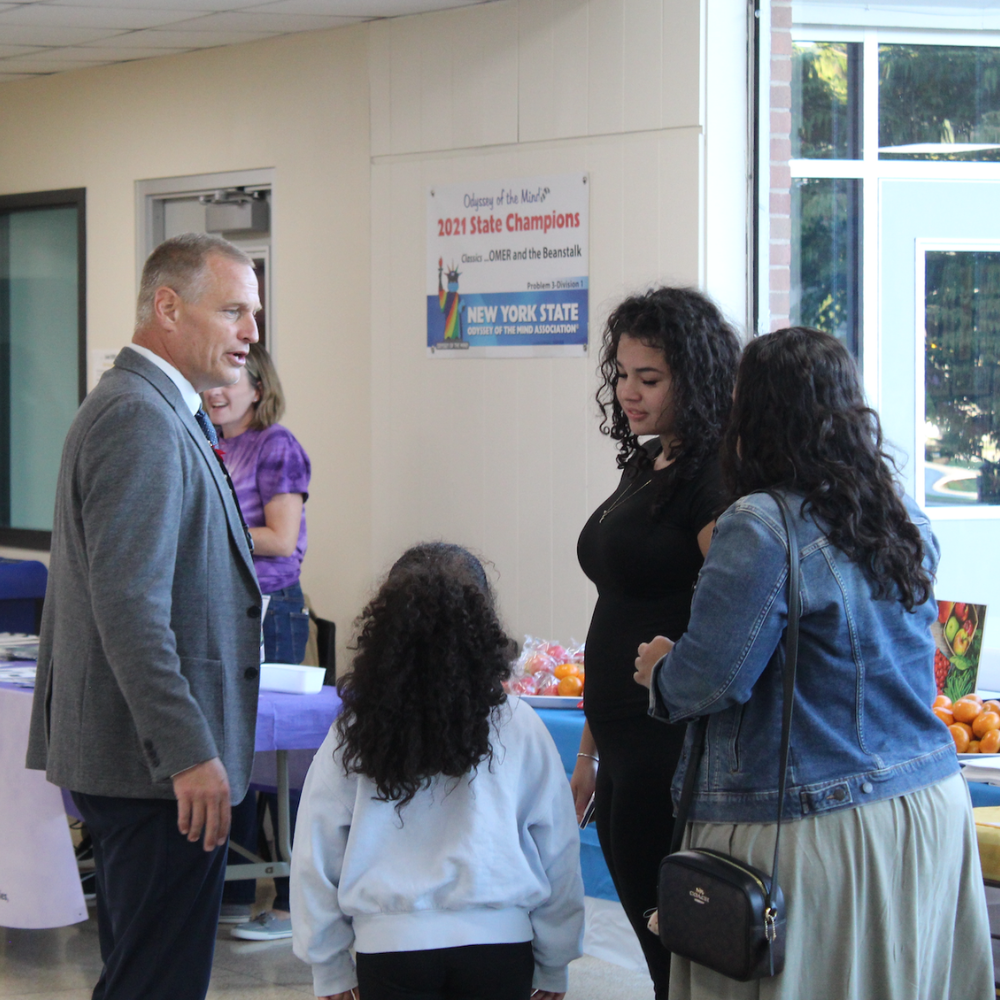 man talking to students and parents in a white hallway 