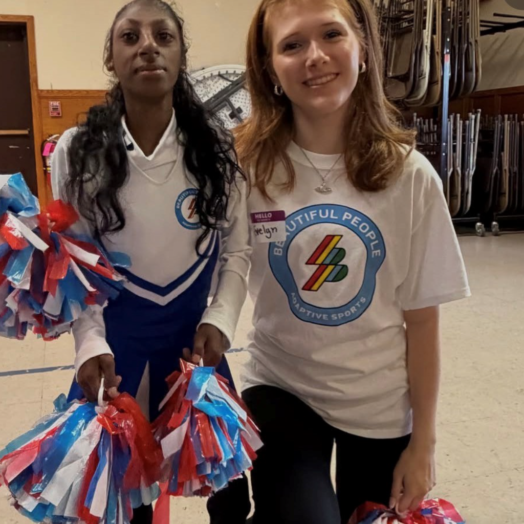two students with white shirts holding colorful pompoms 