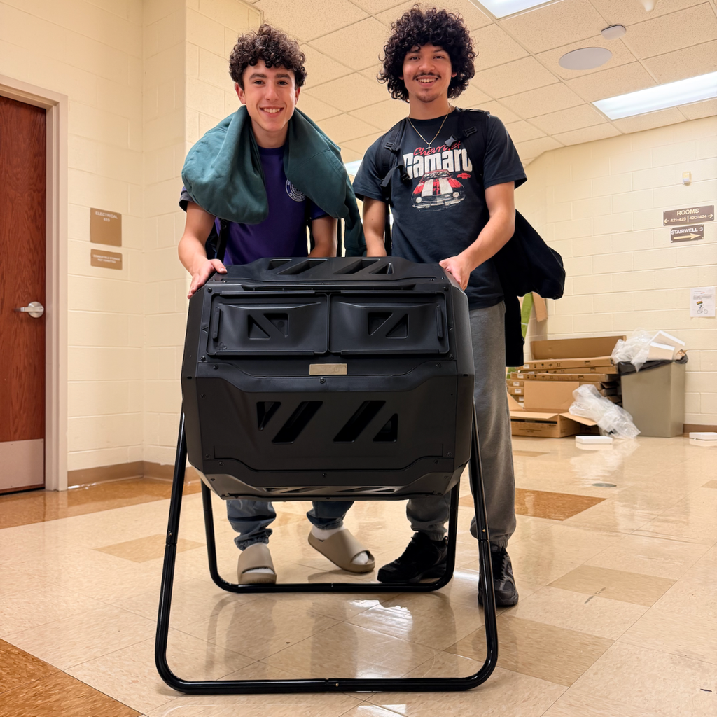 Two boys standing next to a black compost bin in a school hallway.