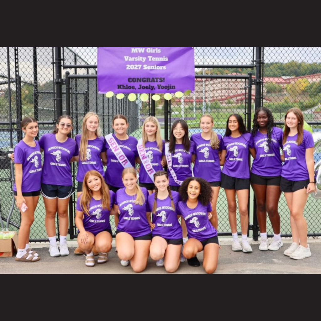Team photo of 11 girls, one wearing a sash, standing on a tennis court with a banner.