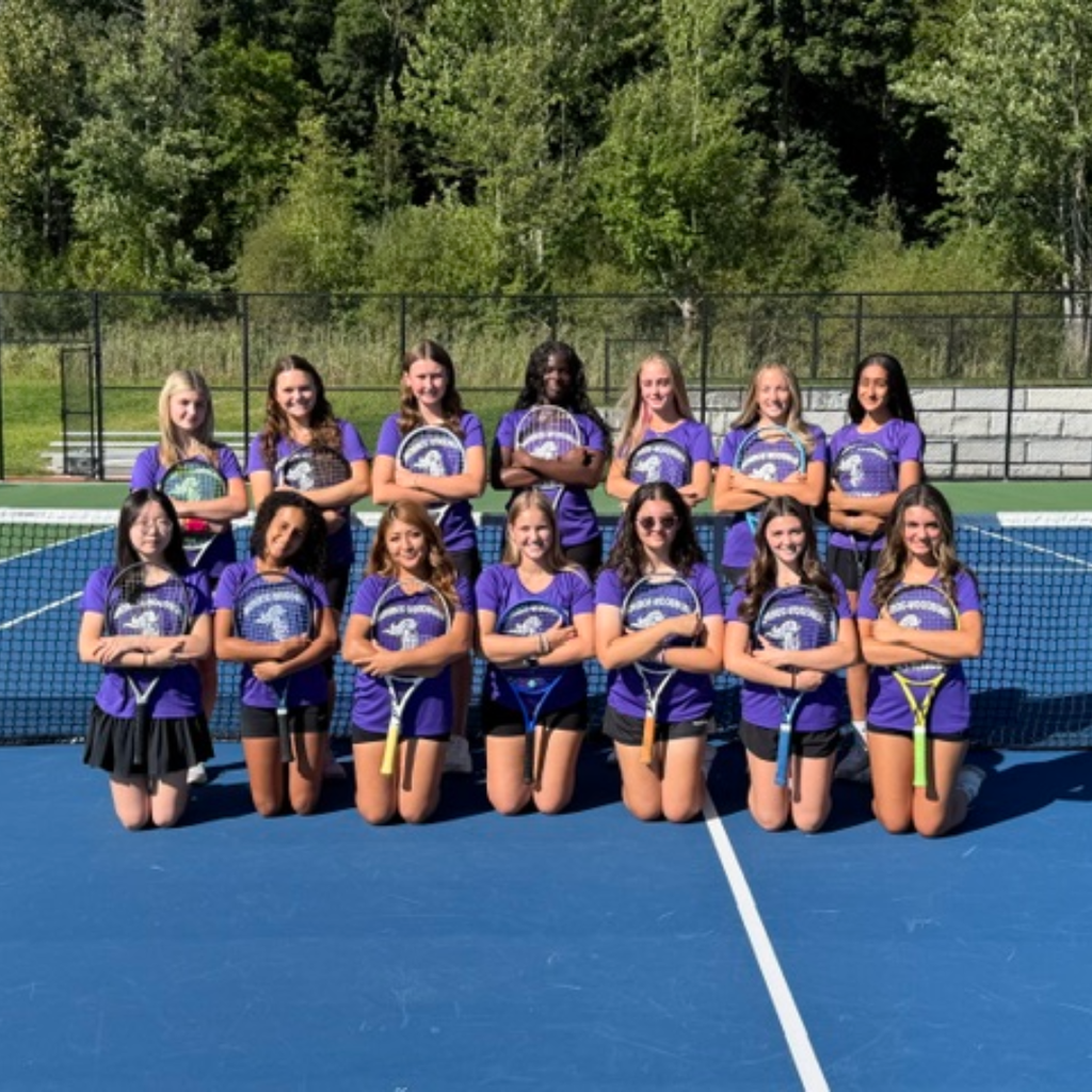A group of female tennis players wearing purple shirts poses for a photo on a court.