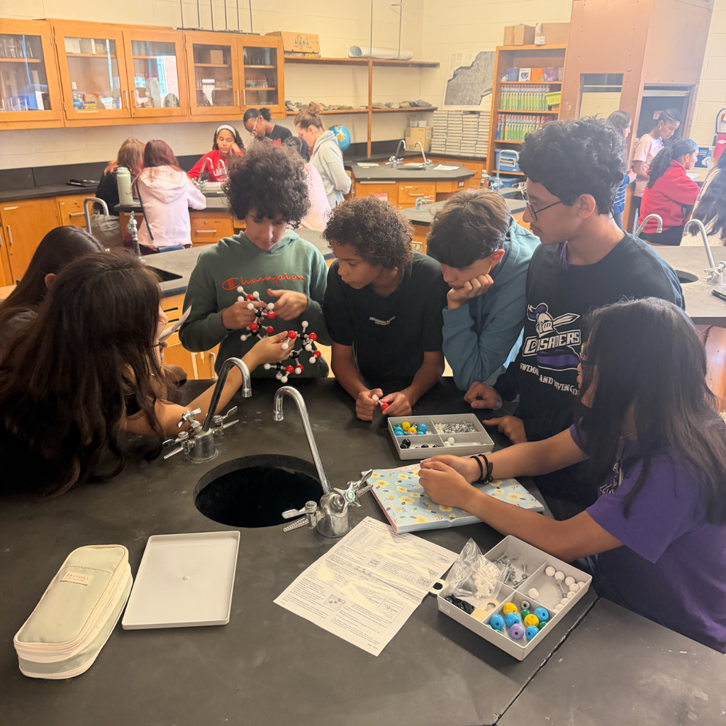 Students gathered around a lab table, working on a project. Various tools and materials are on the table.