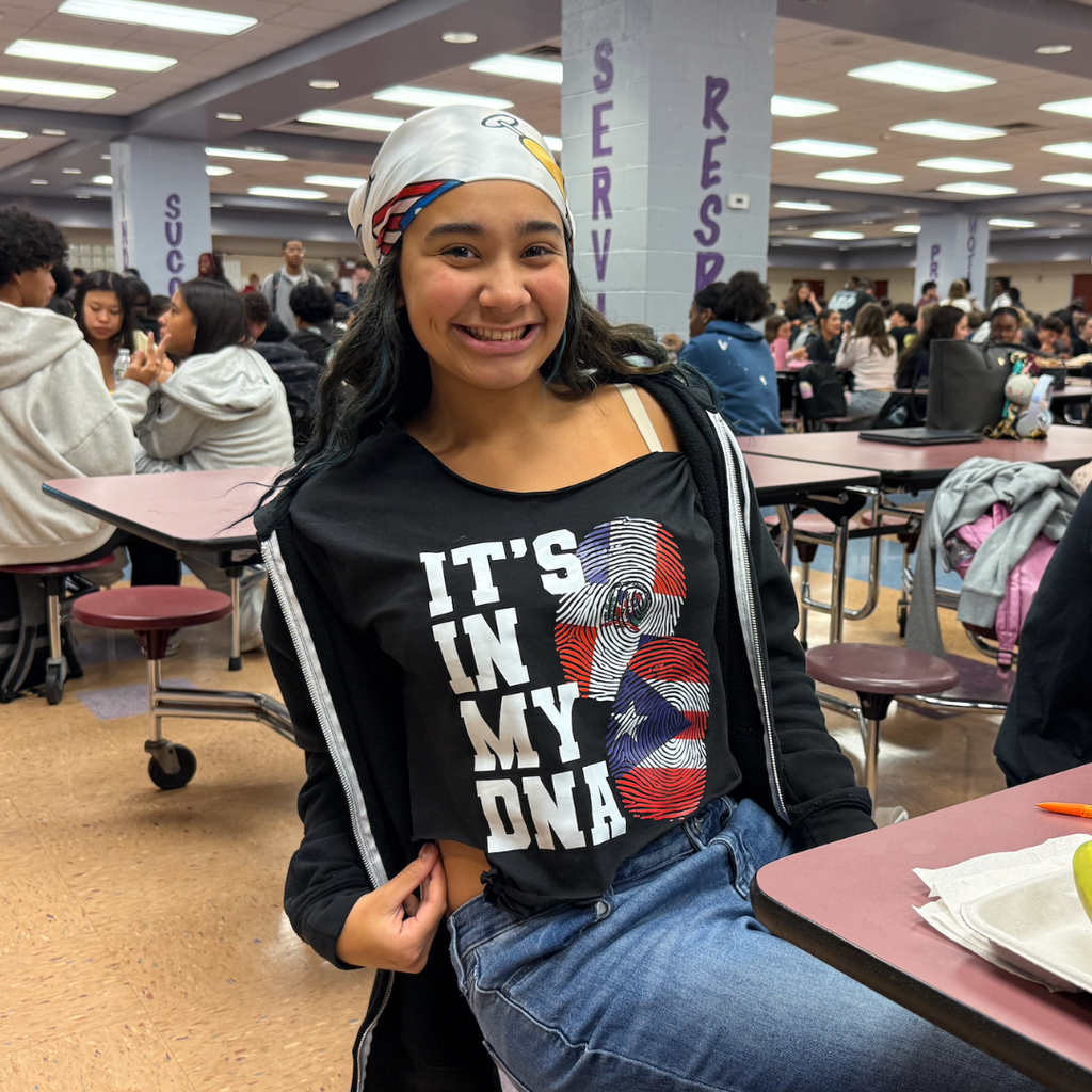 A girl with a bandana, wearing a black shirt with an American flag design, sits in a school cafeteria.