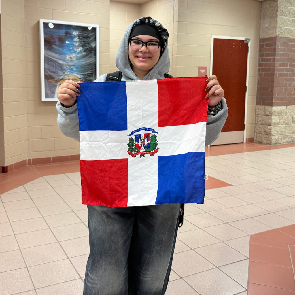 Person in hoodie and glasses holds a Dominican Republic flag in a tiled hallway.