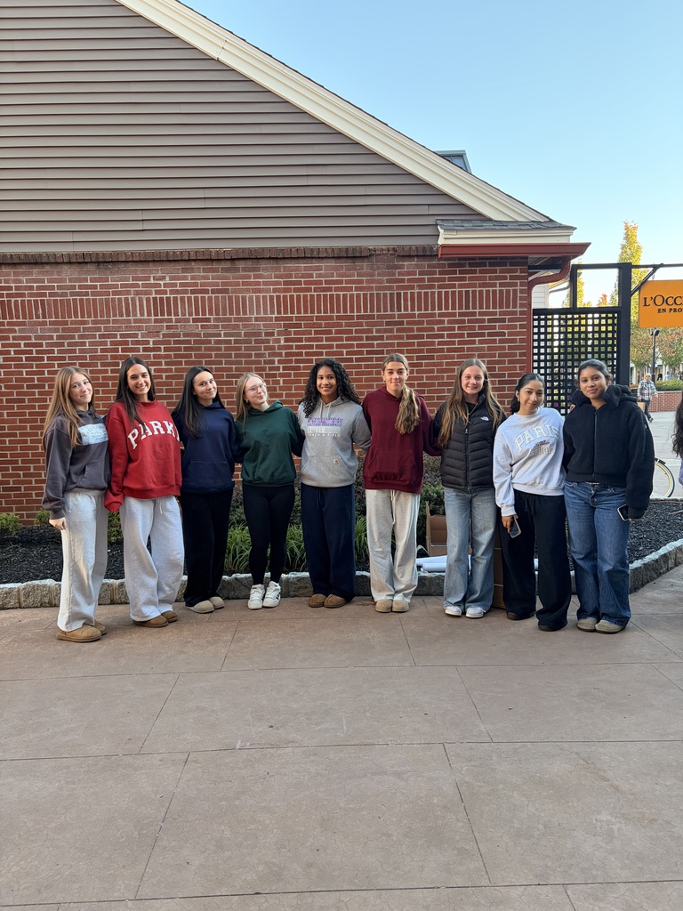 A group of students stands in front of a brick building with an arched entrance.