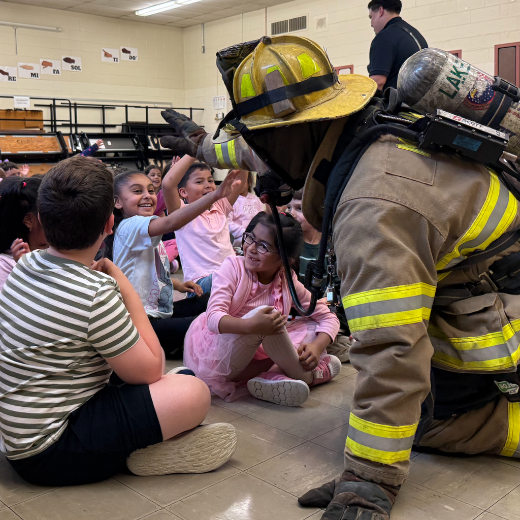 firefighter crawling on floor giving students high five