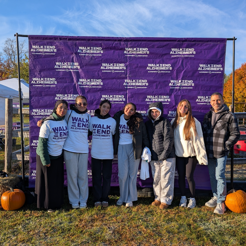 seven people stand in front of a purple banner with the text "WALK TO END ALZHEIMER'S."