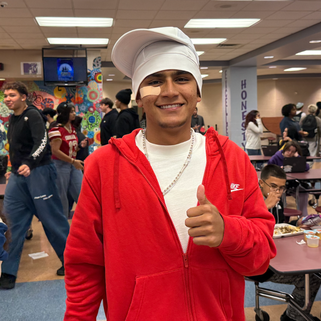 People in a cafeteria, one man in red wearing a baseball hat, giving a thumbs up.