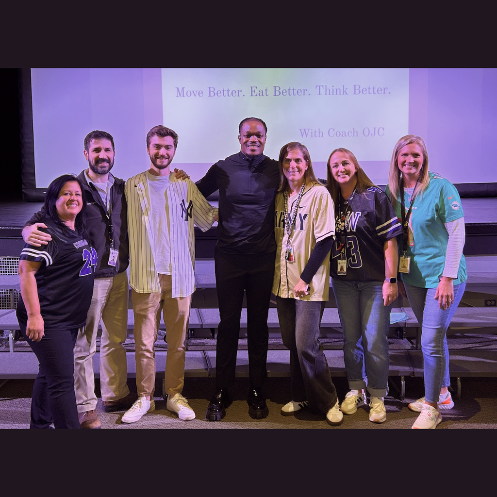 Nine adults in a school auditorium posing for a photo in front of a projection screen.