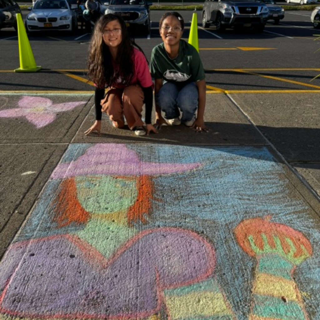 Two children crouch beside a large sidewalk drawing of a girl and a flower.