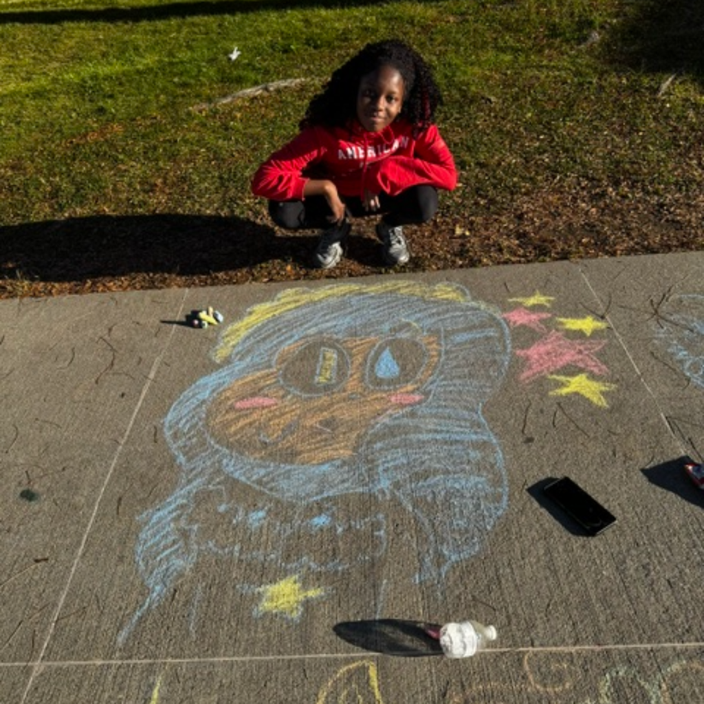 Person kneeling beside sidewalk chalk drawing of a face and eyes, one eye crying, with stars.