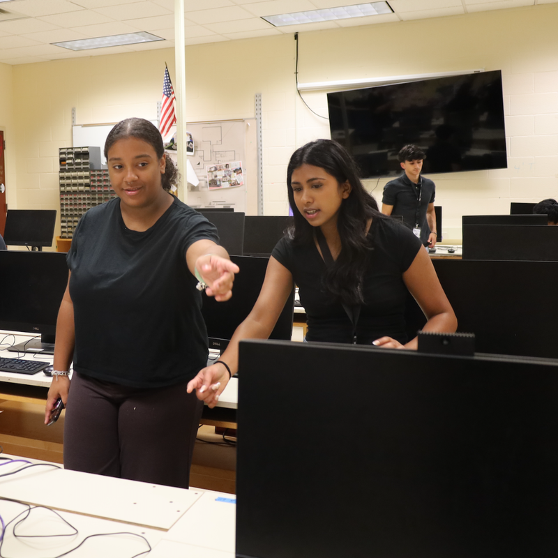 two students with black shirts pointing to computers