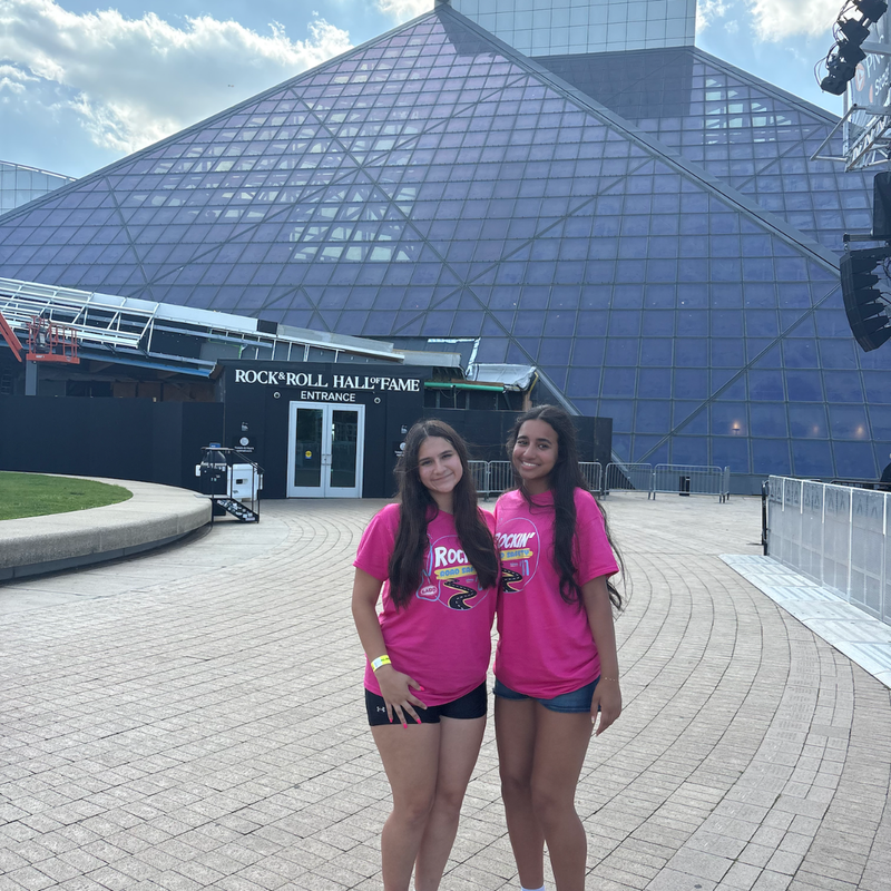 two girls with pink shirts standing in front of a triangle glass building