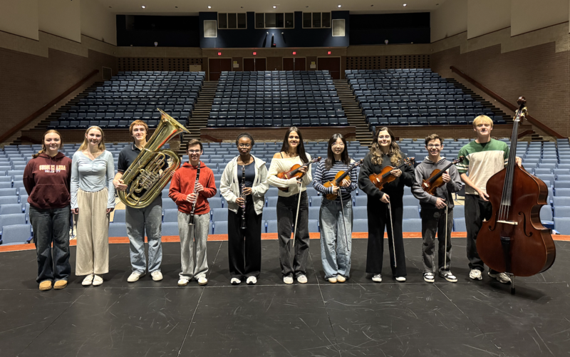 10 musicians standing on a stage in an empty auditorium