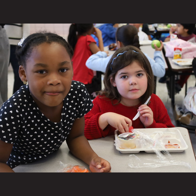 two girls sitting at a table eating apples and carrots