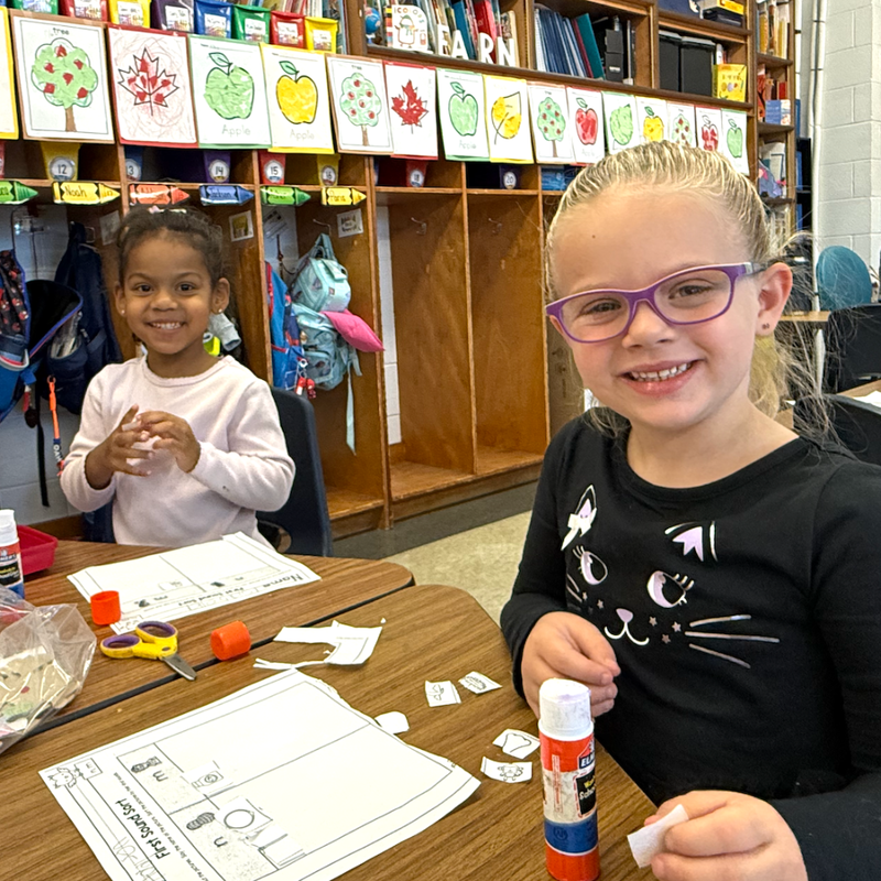 girl with black dress and pink glasses smiling with girl with pink shirt