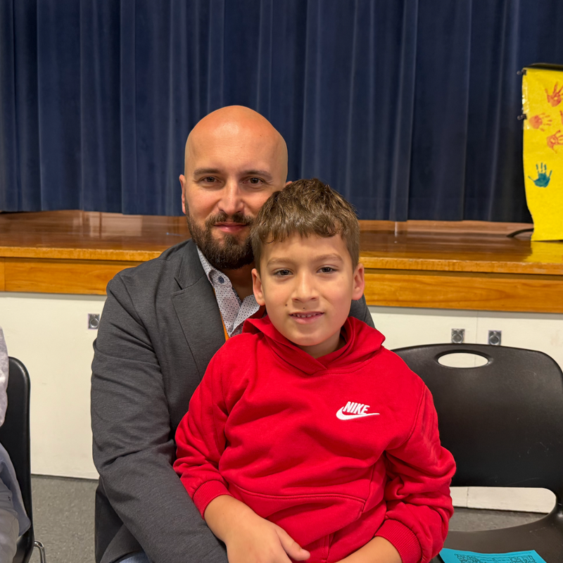 man with grey jacket sits with boy with a red shirt