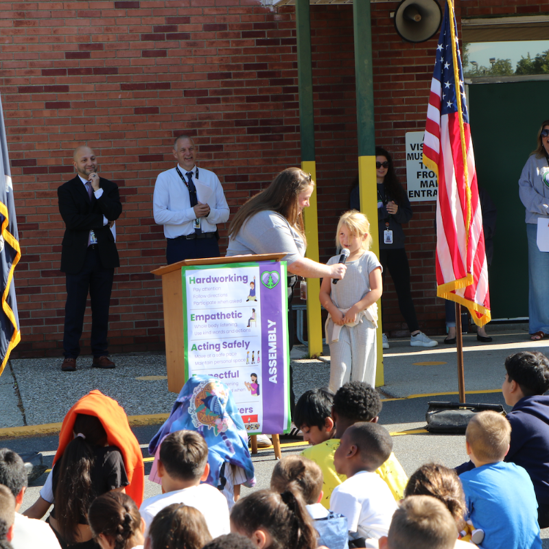 student standing at a podium in front of an audience with an American flag