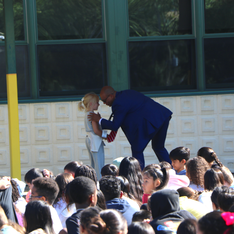 man with blue suit standing with student in front of audience