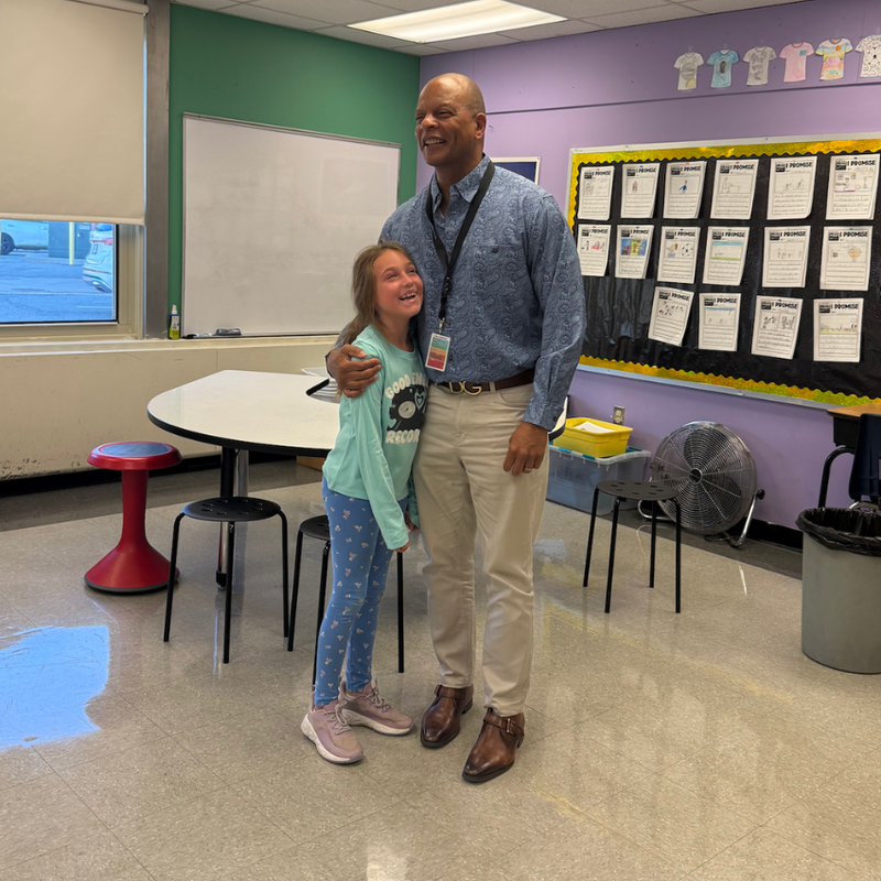 man in a blue shirt hugging student in blue shirt