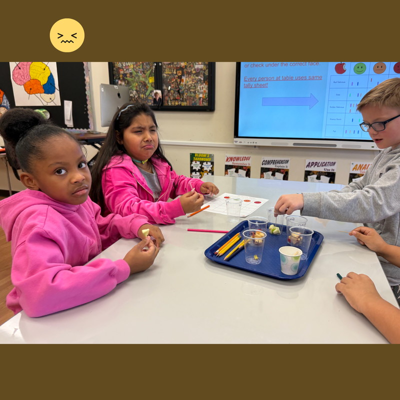 students with pink shirts sitting at a white table with apple slices