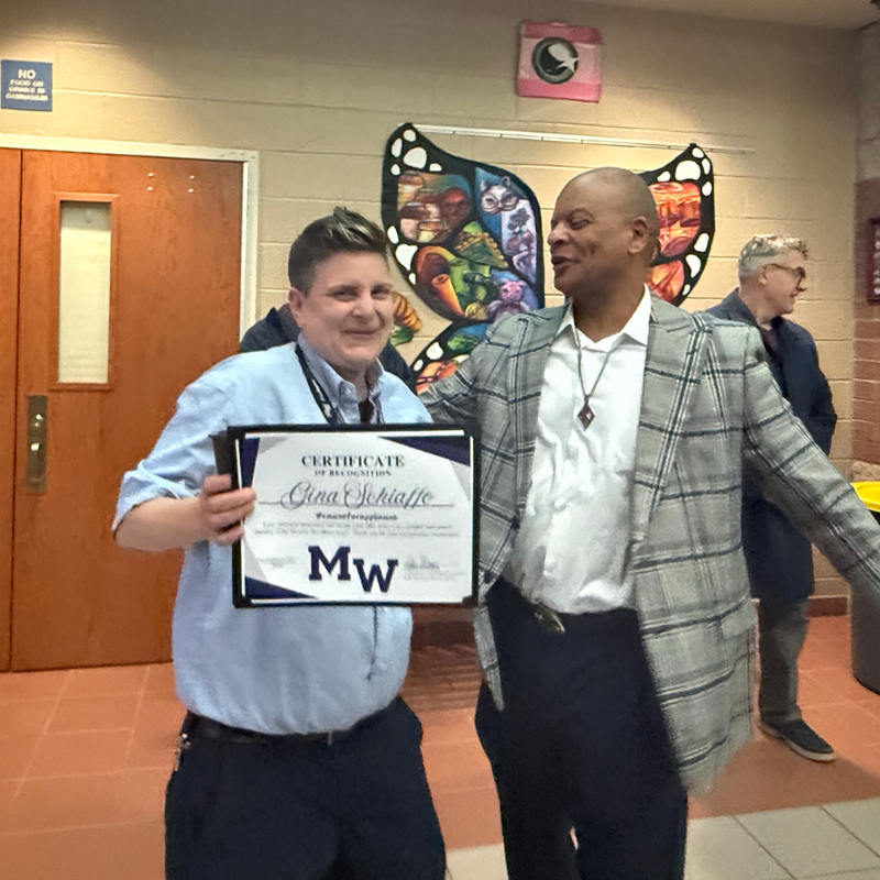woman with blue shirt holding certificate next to man with checkered suit