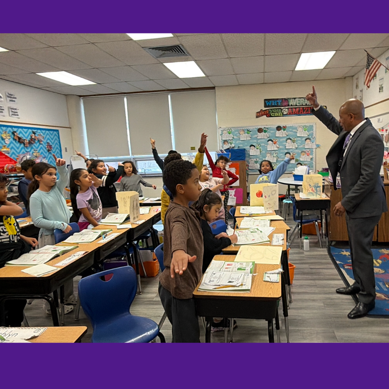 man standing with hand up and students have hands out