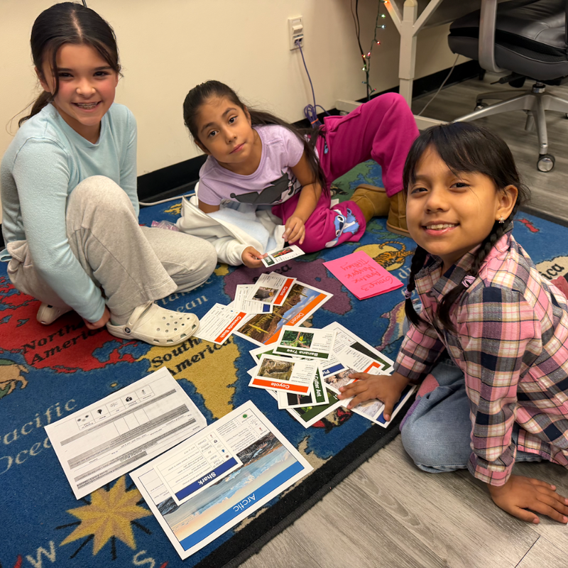three students sitting on a rug with papers