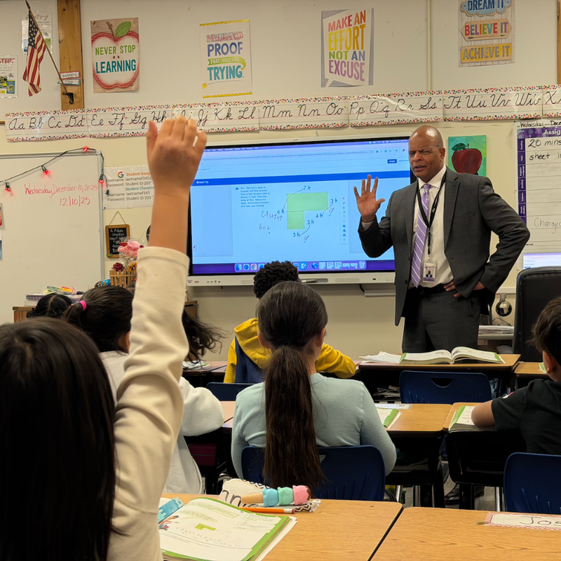 man standing in front of classroom and students raising their hands