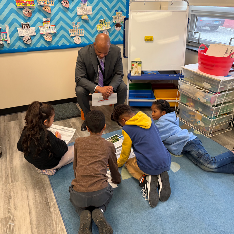 man sitting on chair with four students sitting on the floor