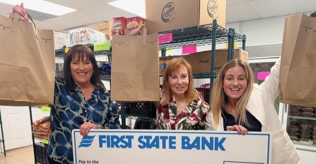 Three women holding a check and holding up grocery bags