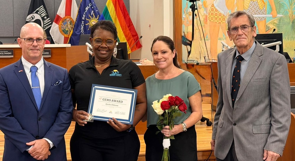 Ayesha Osborne receiving GEM Award from superintendent and board chair at school board meeting