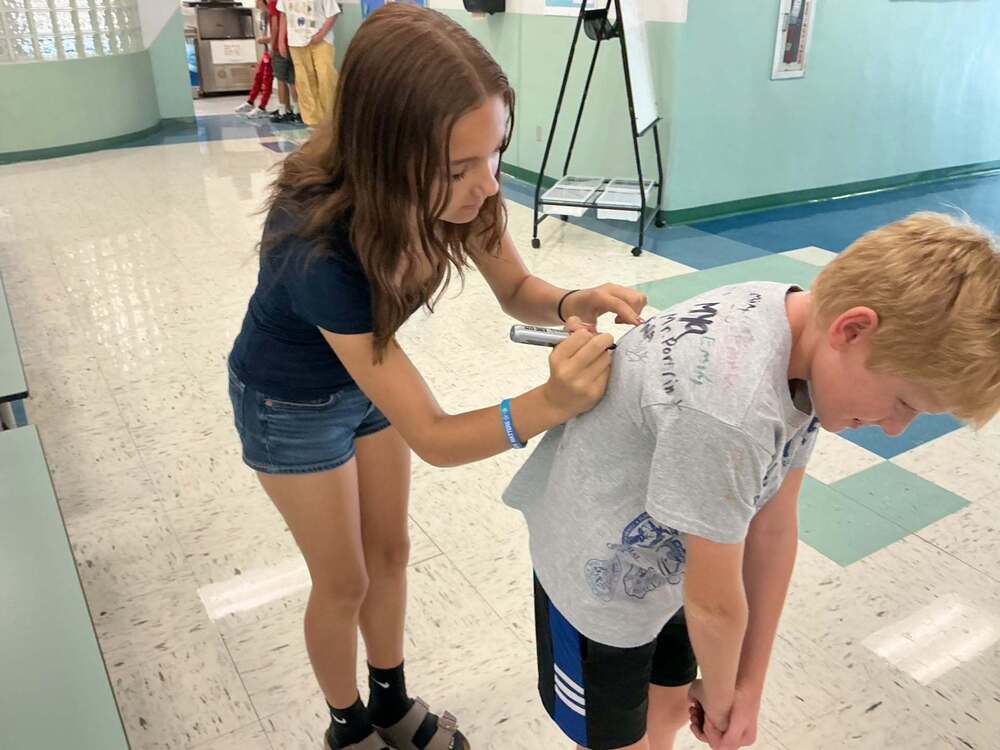 One student signing another student's shirt during sign up to be kind week