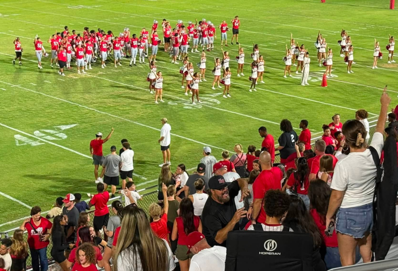 Players and cheerleaders on the field with crowd cheering
