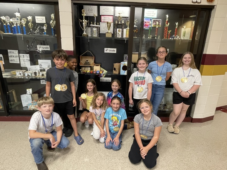 students in front of trophy case with winning cars 