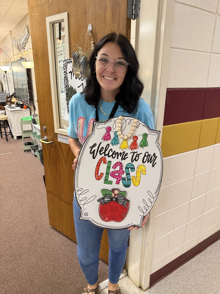 Mrs. Justice holding her DK Designs door hanger that says welcome to our class