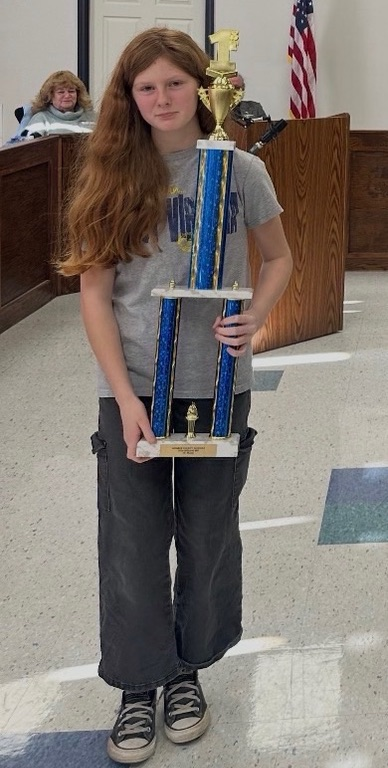 student holding a large trophy in a gray shirt and gray pants.  
