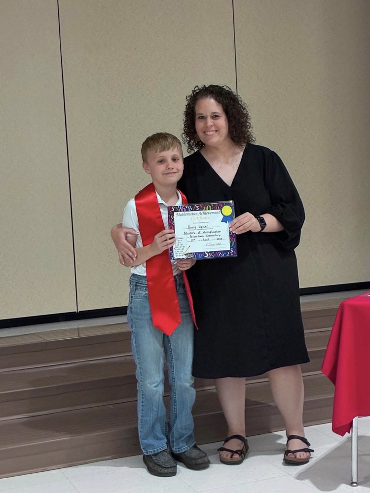 student in blue jeans with Miss Wills putting on a red sash