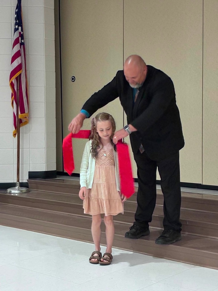 student in Perice with Dr. Conaway putting on a red sash